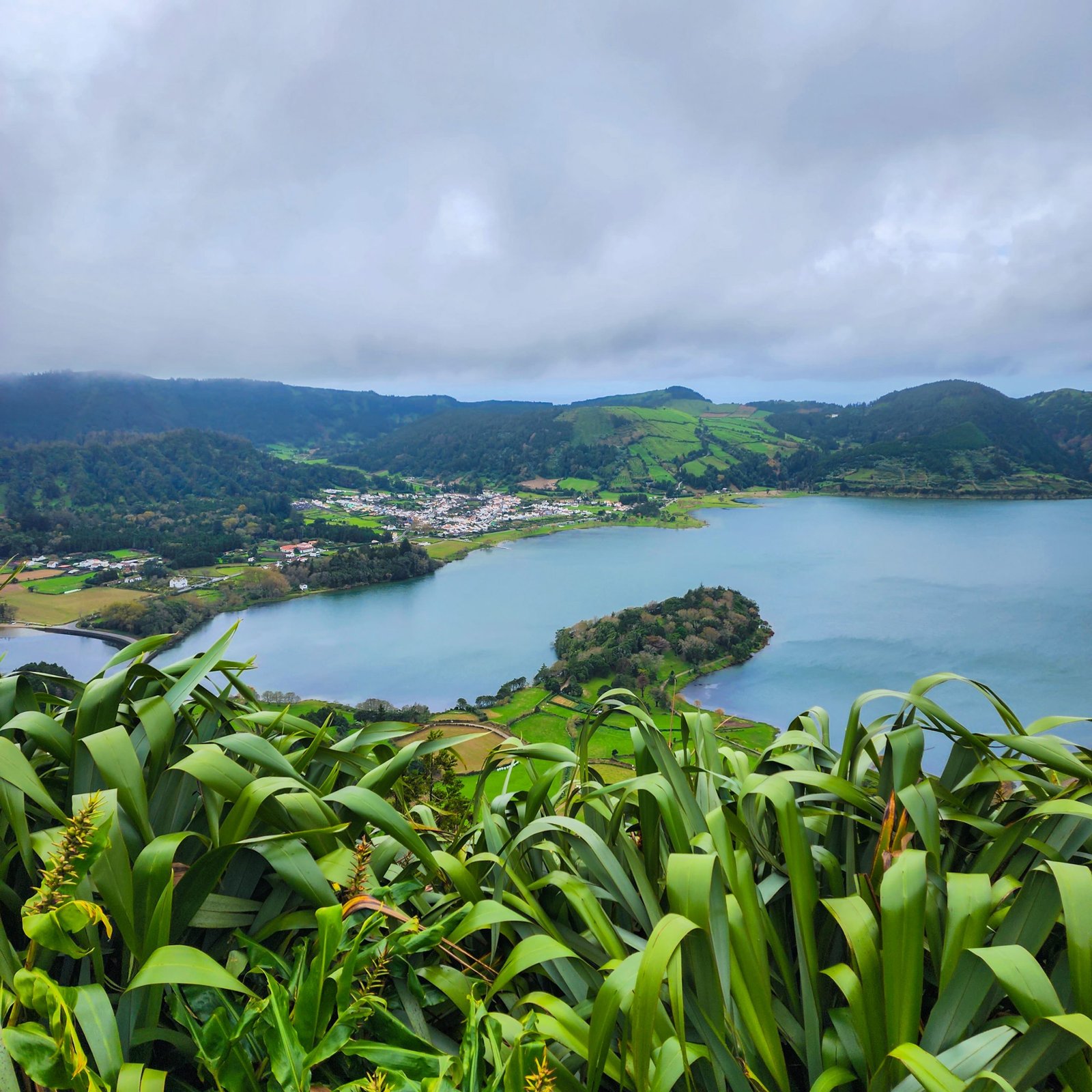 View of Crater Lakes in the Azores with a blue lake and green forest and farmland in the distance