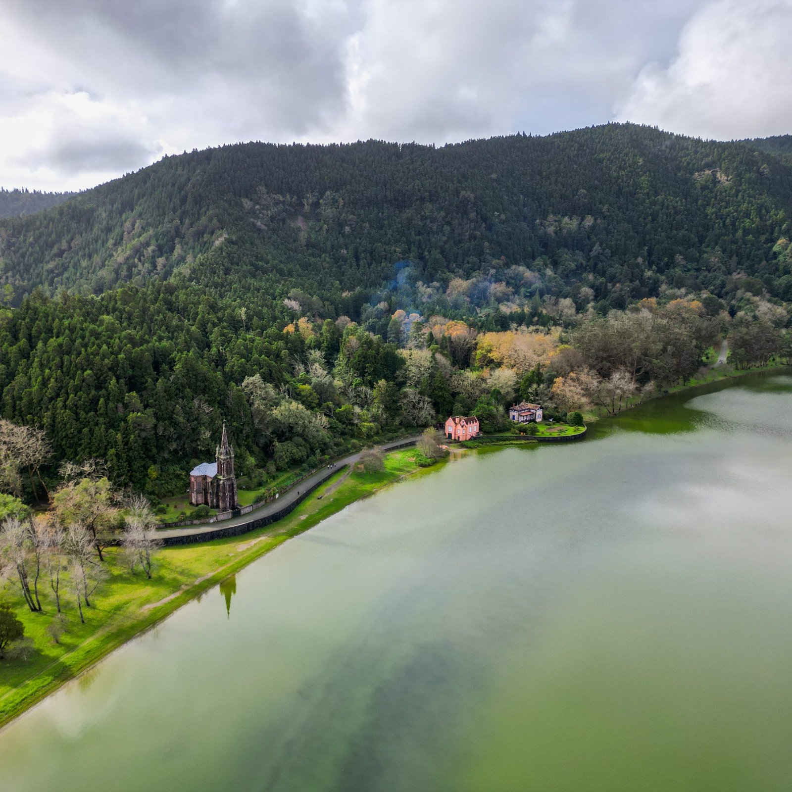 Drone photo of a church and pink house on the edge of a green lake