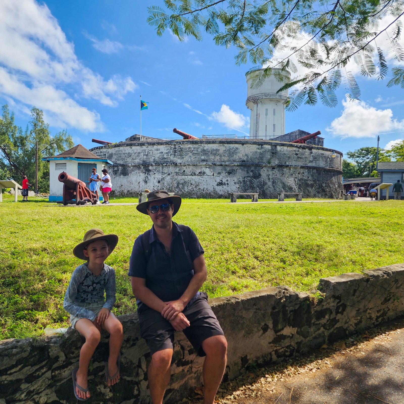 Father and Daughter sitting on a wall with a fort with cannons in the background