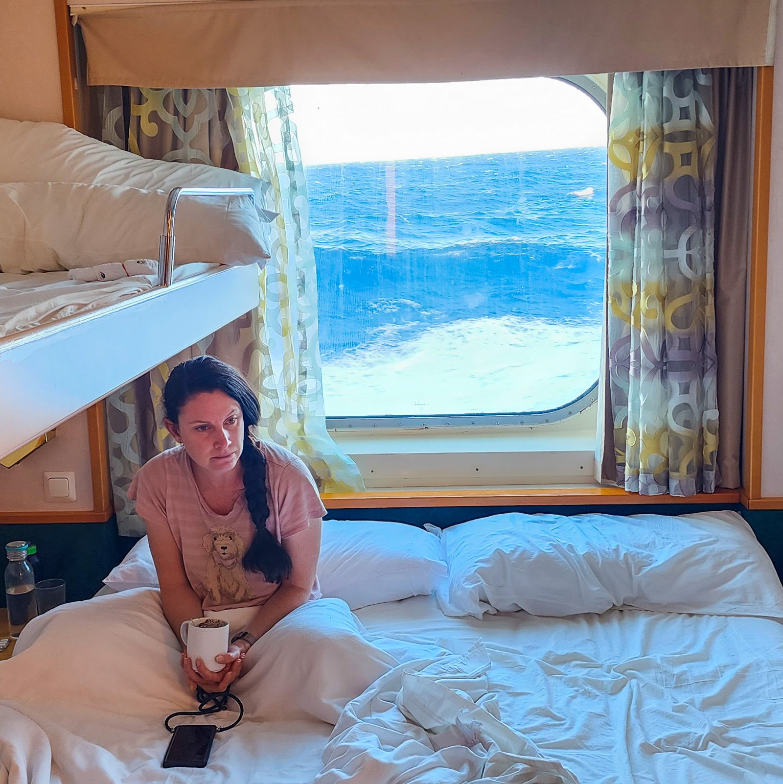 Woman sitting in bed seasick with the ocean waves in the window in the background